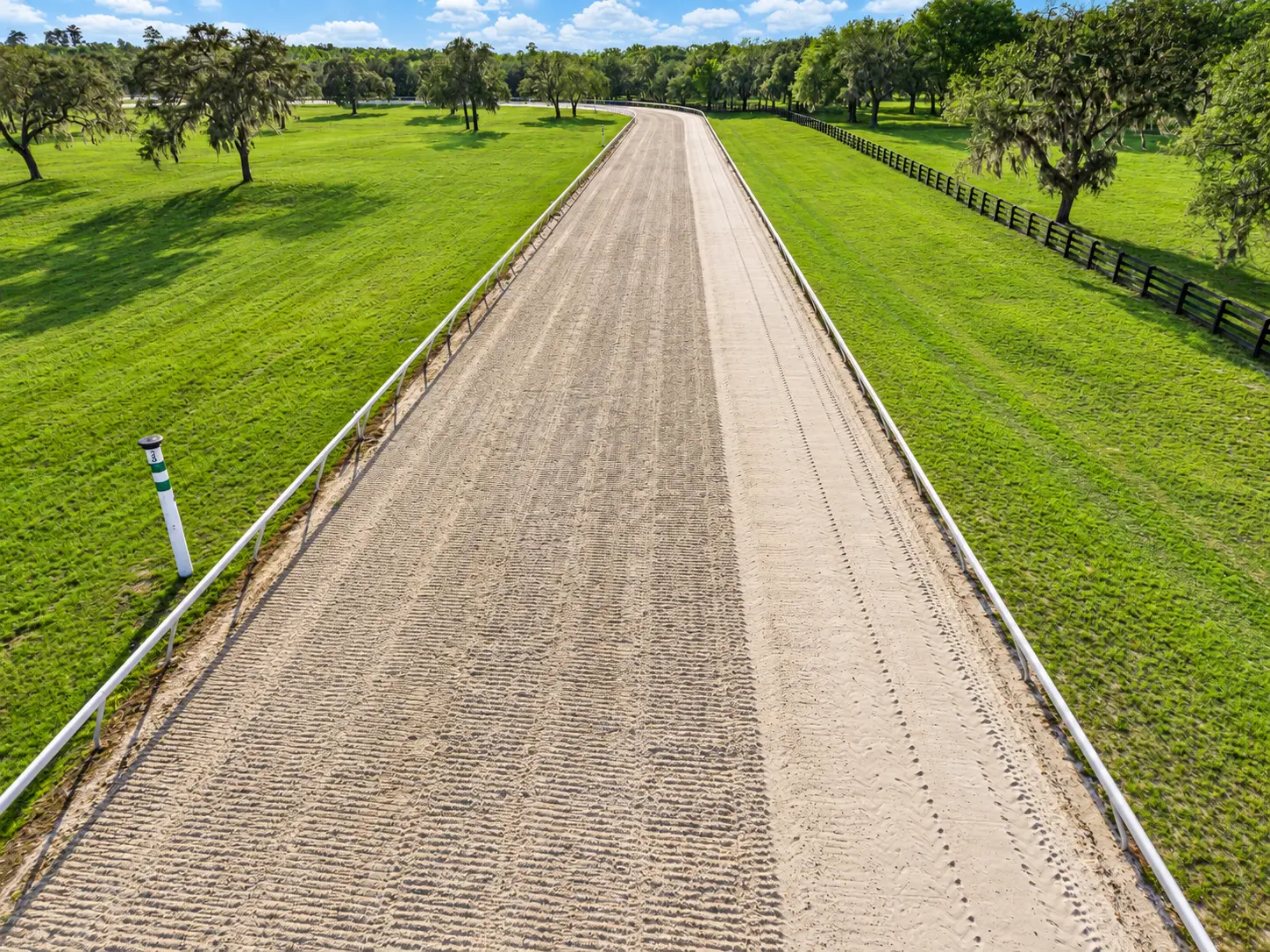 Aerial photo looking down the dirt training track, white rail on the inside