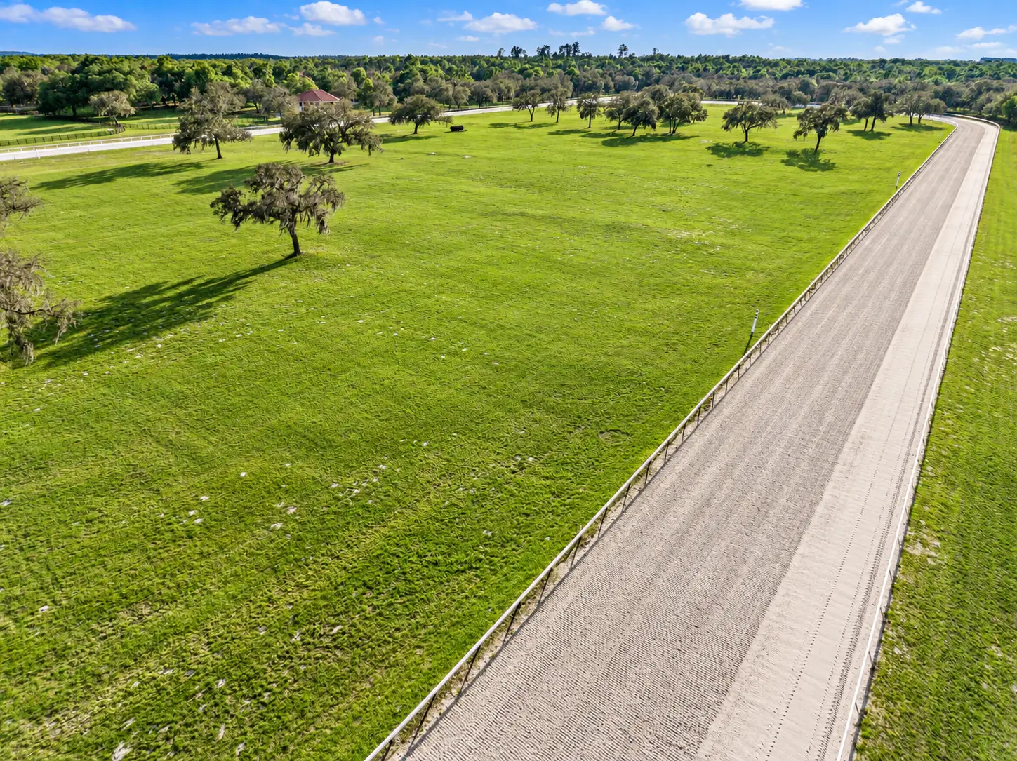 Aerial photo looking along the groomed dirt straightaway with distance marker posts on the inner rail and the oak-studded infield