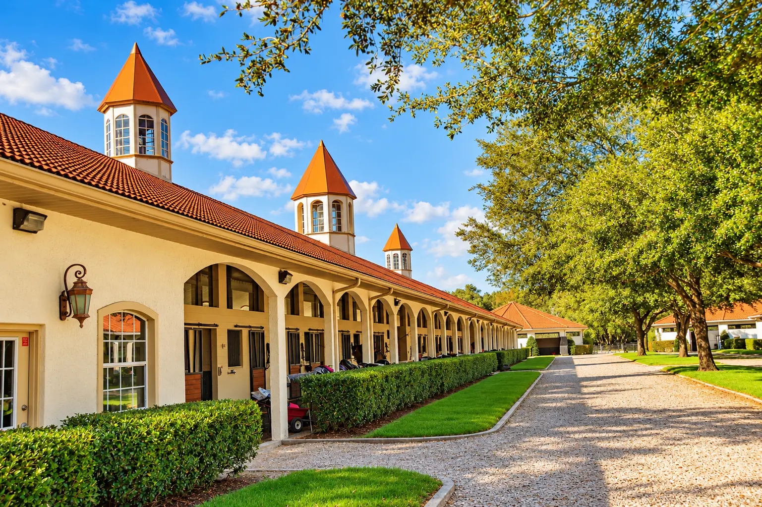 The trainer blocks at GoldMark Farm with the office — the arched stall row and gravel lane under the cupolas