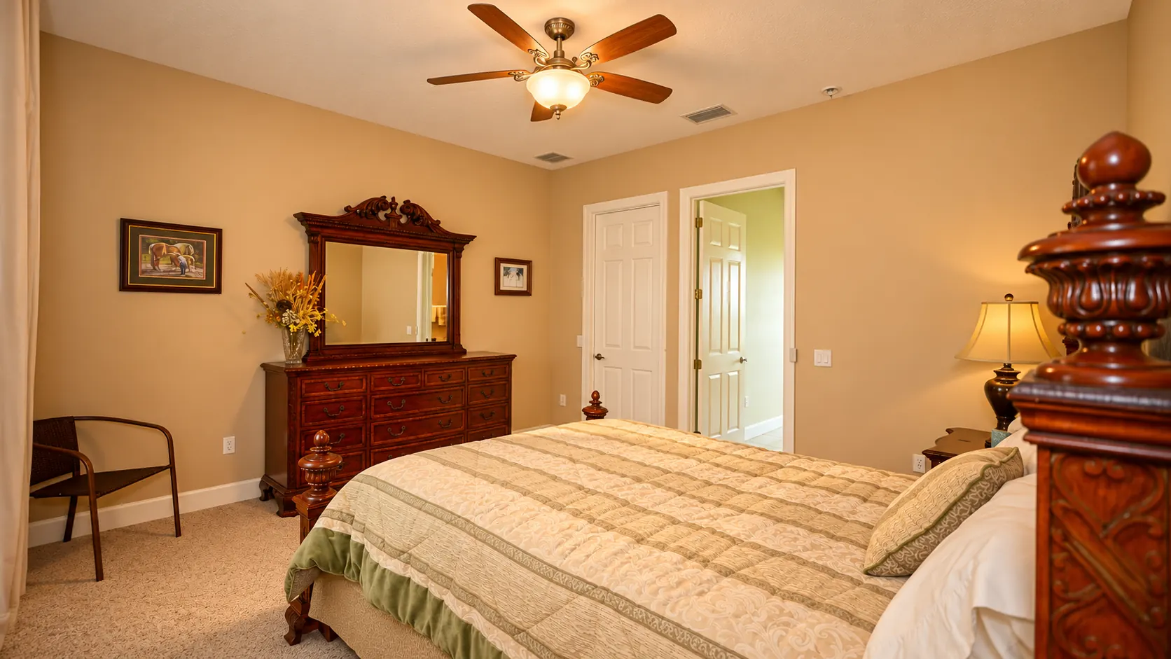A second bedroom in the viewing apartment with a carved four-poster bed, matching dresser and mirror, and a ceiling fan