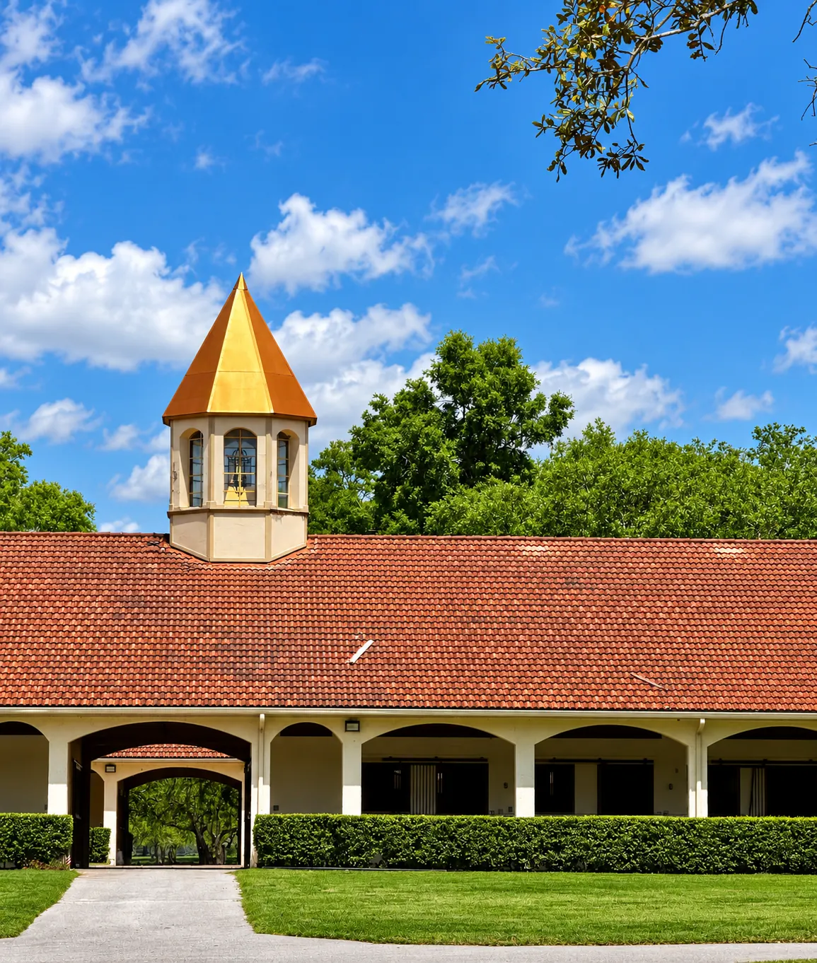 The training barn under a bright blue sky — terracotta roof, arched walkway and the gold cupola above the entrance