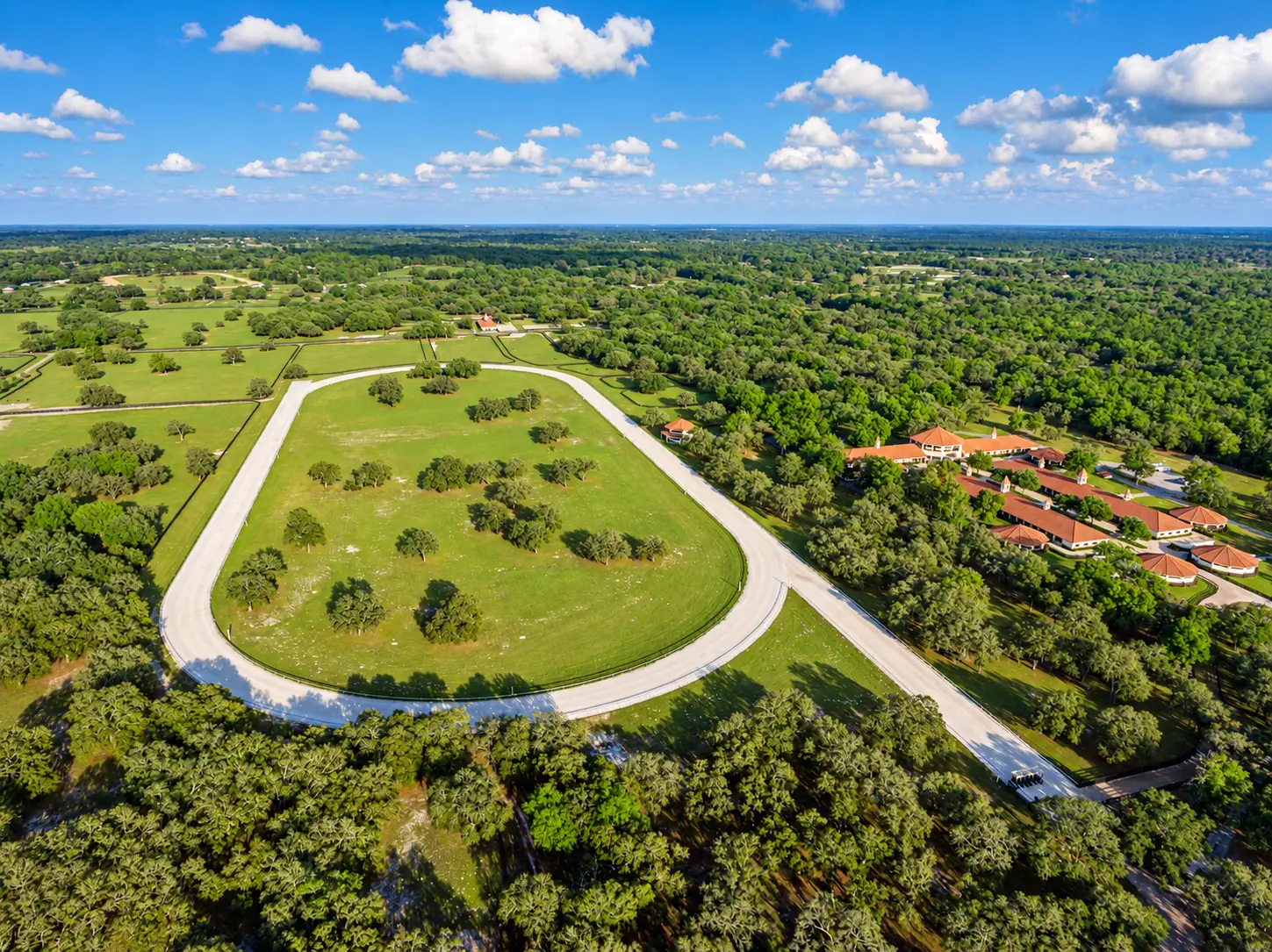 Wide aerial photo of the farm with the training track loop and the barns among green fields