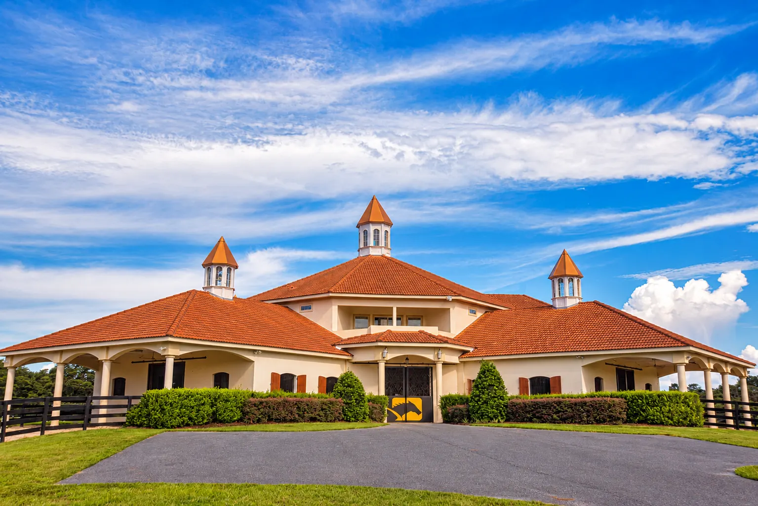 The GoldMark mare barn at golden hour with cream stucco walls, arched walkways, terracotta roofs and three cupolas above the gated driveway