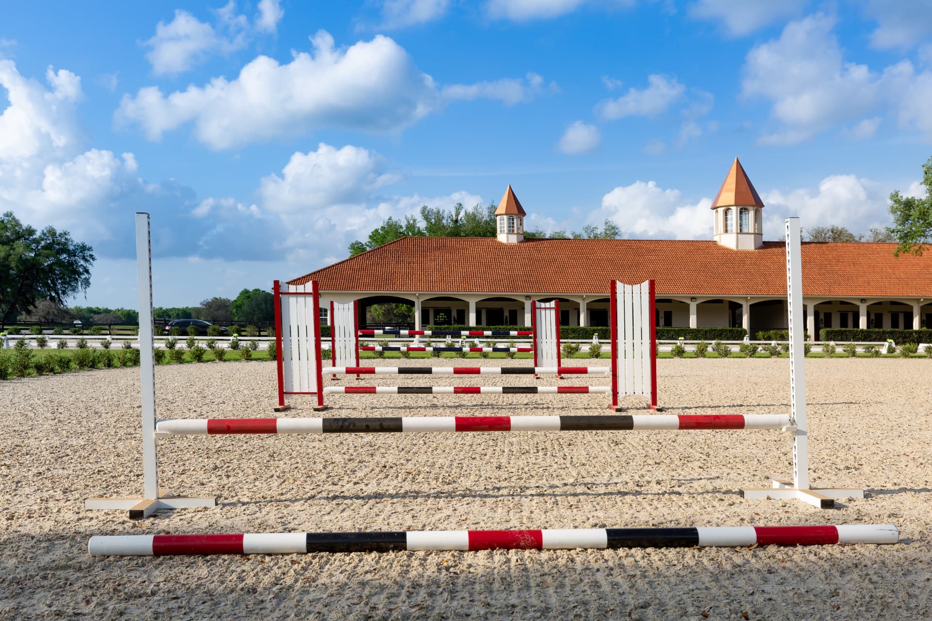 The GoldMark jumping arena with jump standards and the twin-cupola barn beyond